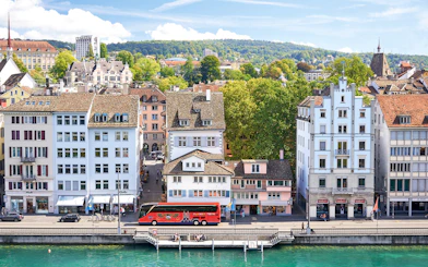 Historic buildings along the Limmat River in Zurich, with a tour bus parked nearby.