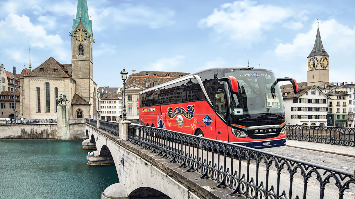 Tour bus crossing a bridge in Zurich with historic church in background.