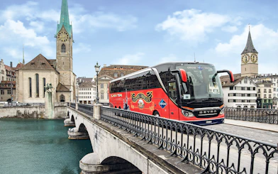 Tour bus crossing a bridge in Zurich with historic church in background.