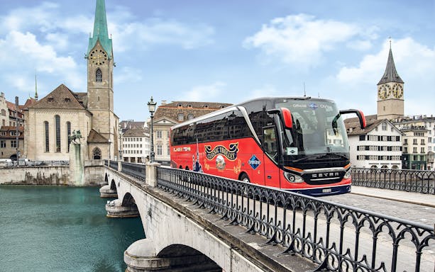 Tour bus crossing a bridge in Zurich with historic church in background.