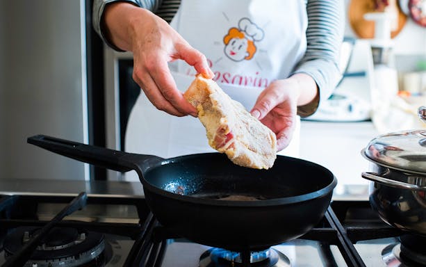 Person preparing breaded cutlet in a private cooking class in Milan kitchen.