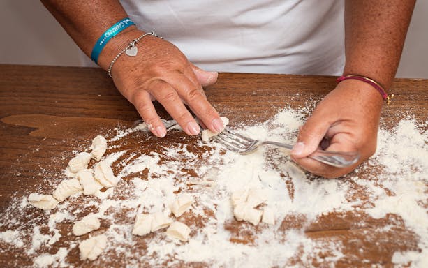 Hands shaping gnocchi dough with a fork during a private cooking class in Milan.