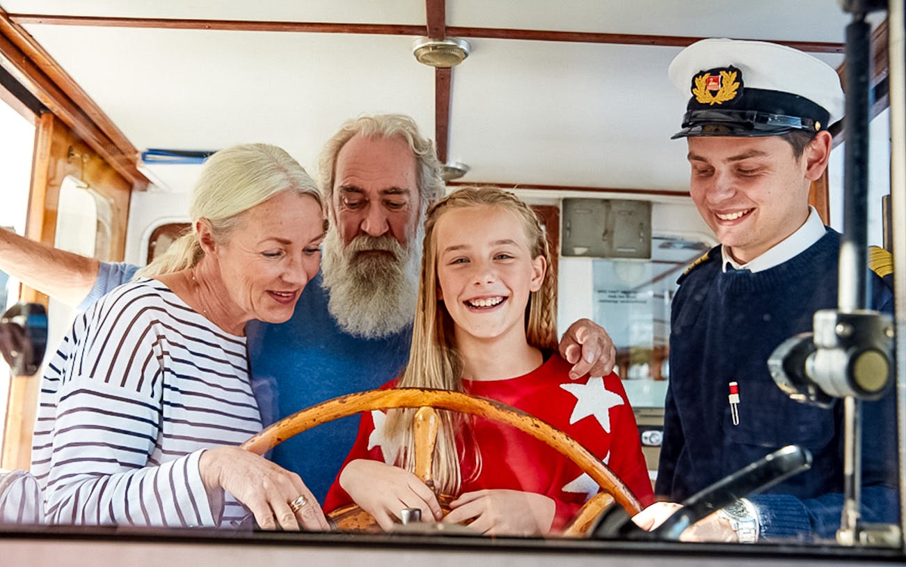 Family steering a boat with a captain on a sightseeing canal tour along the Alster.