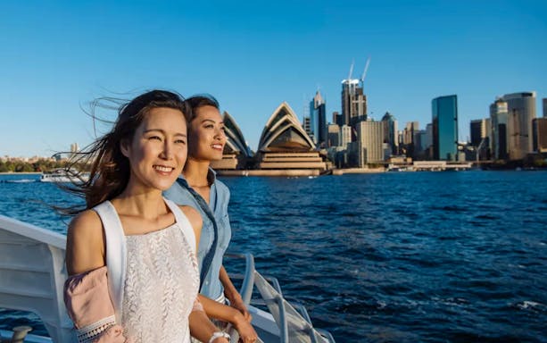 Two people enjoying a boat tour with the Sydney Opera House in the background.