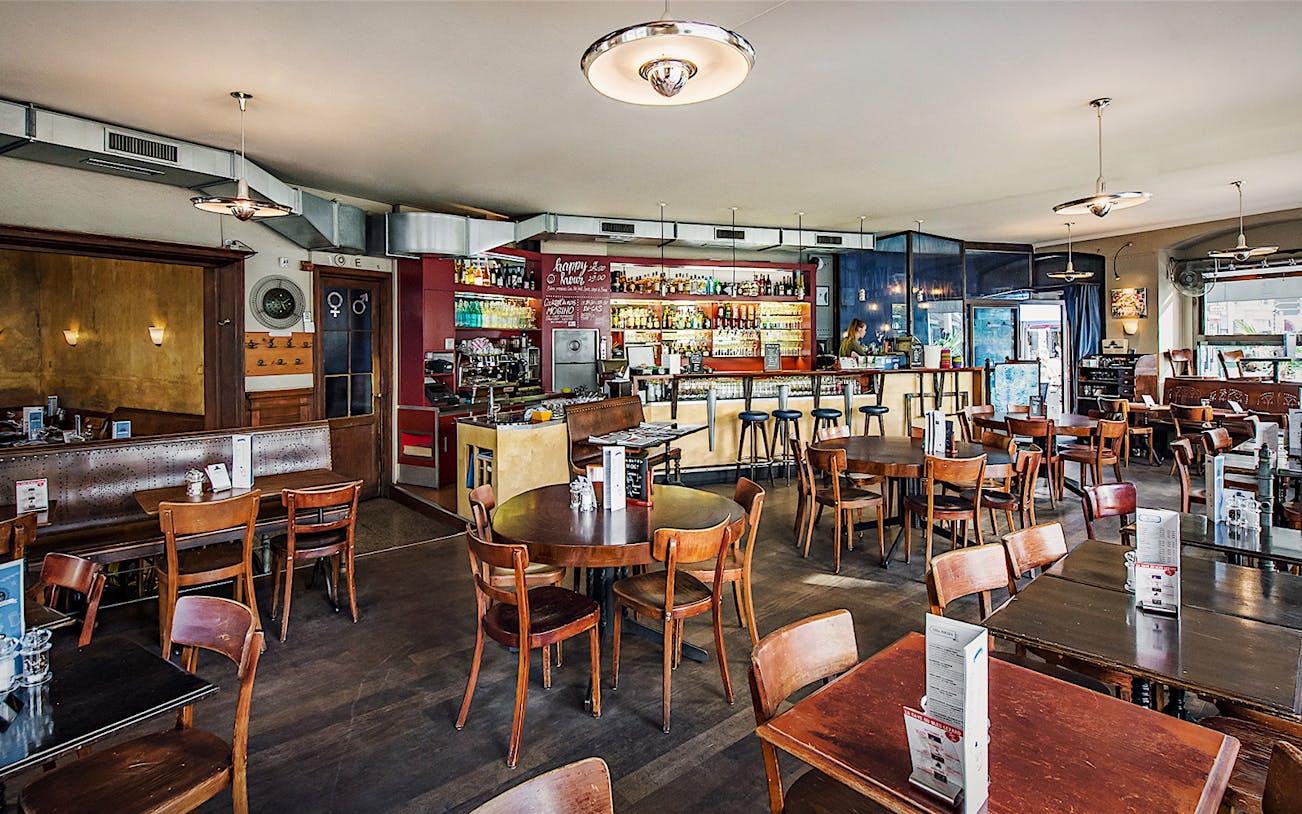 Lausanne café interior with wooden tables and chairs, bar counter, and menu displays.