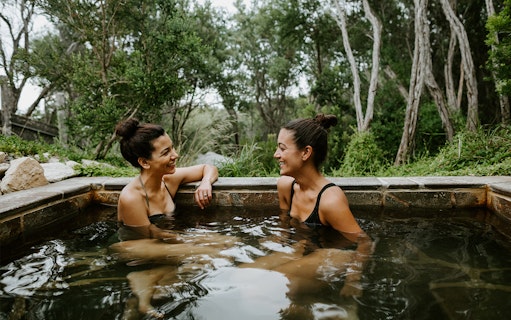 Two people relaxing in a hot spring at Peninsula Hot Springs, surrounded by lush greenery.