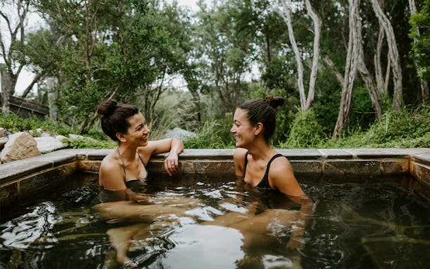 Two people relaxing in a hot spring at Peninsula Hot Springs, surrounded by lush greenery.