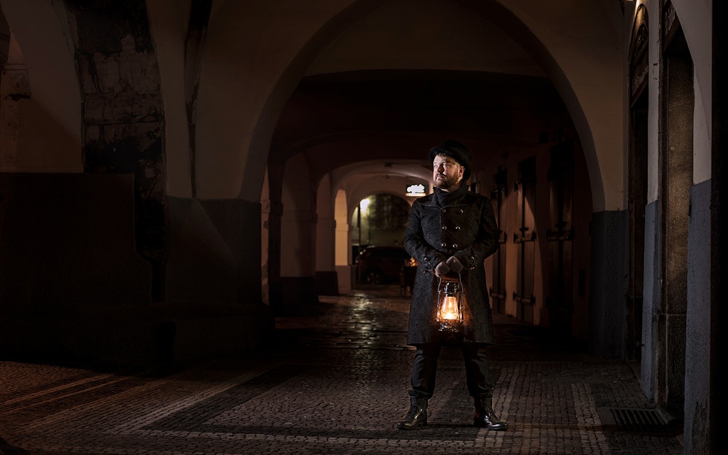 Guide holding lantern in Prague's Old Town during night-time ghost tour.