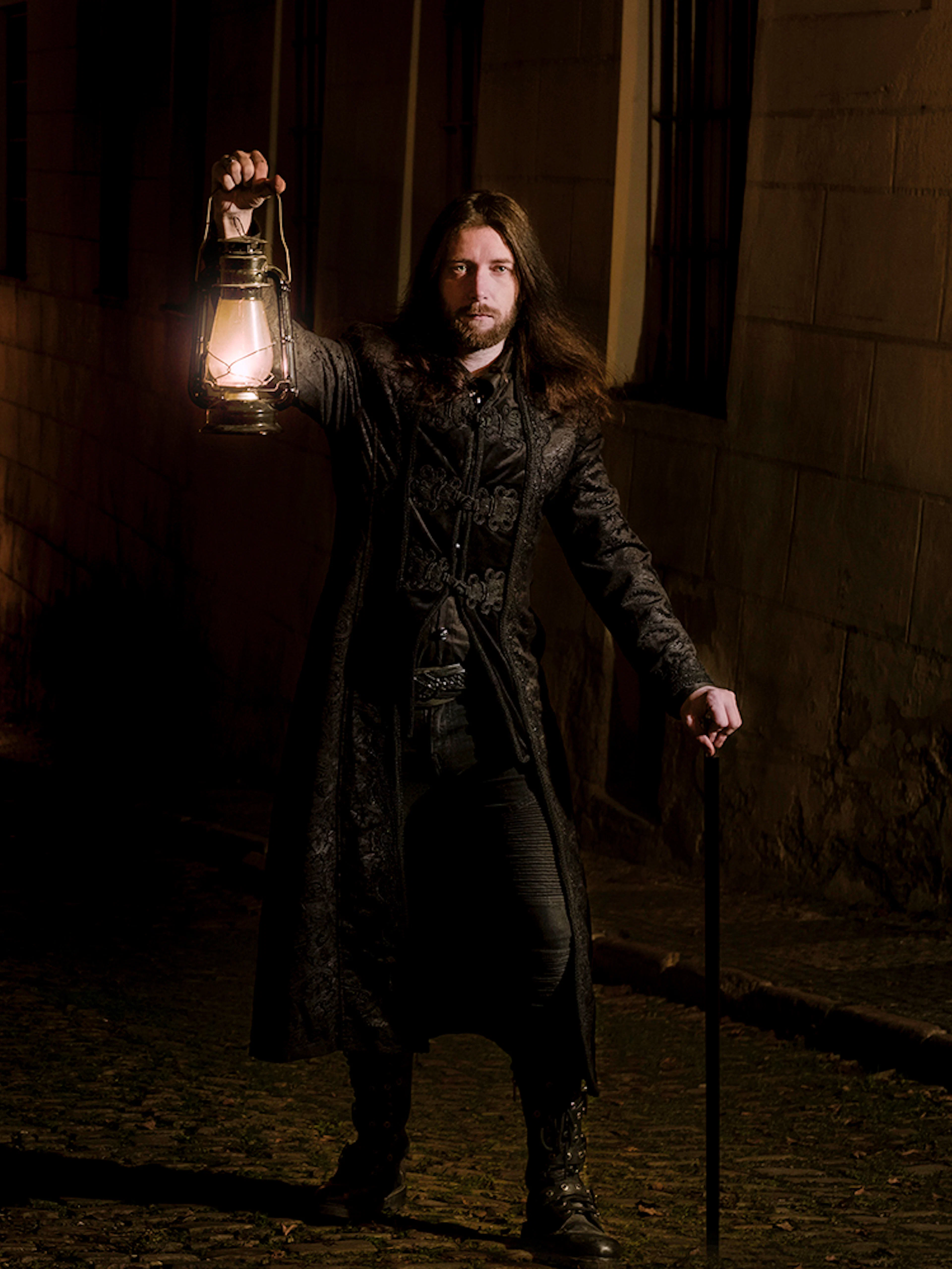 Man holding lantern in dark alley during Prague's Old Town ghost tour.