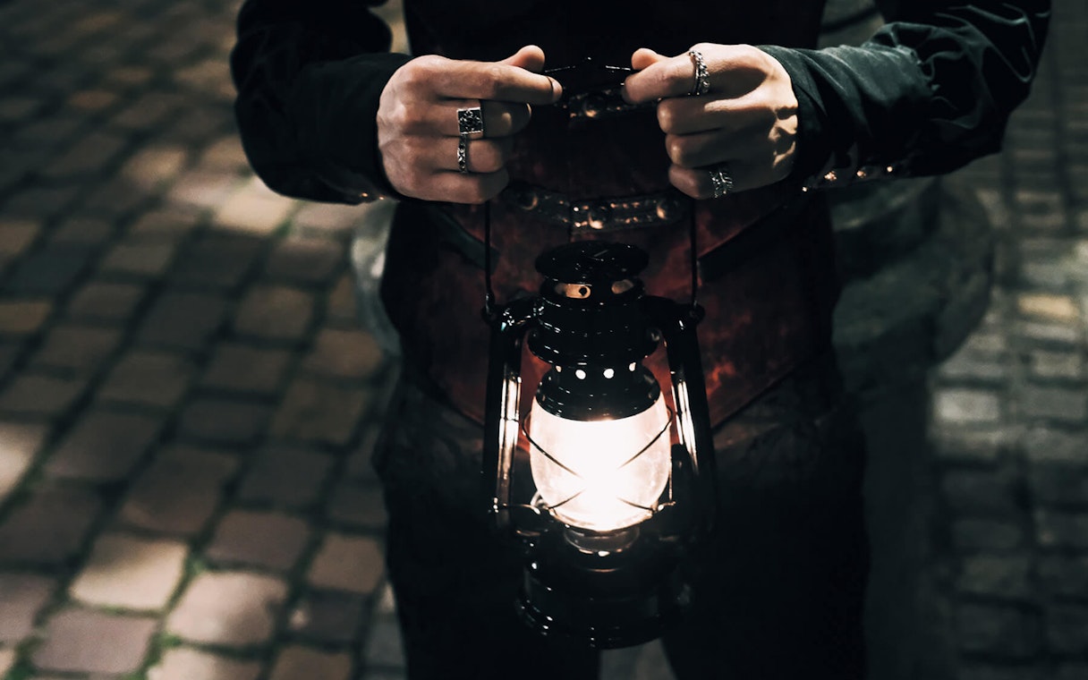 Person holding a lantern on cobblestone street during Prague's Old Town ghost tour.