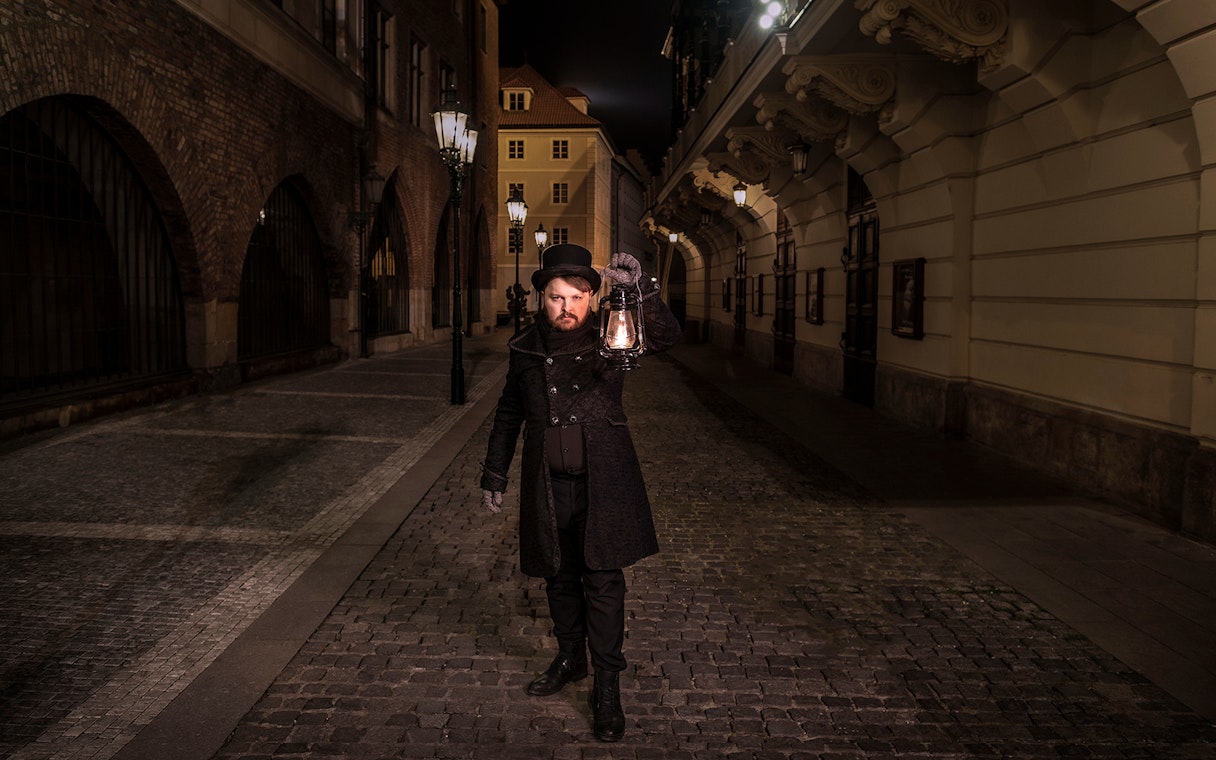 Guide holding lantern on cobblestone street during Prague Old Town ghost tour.