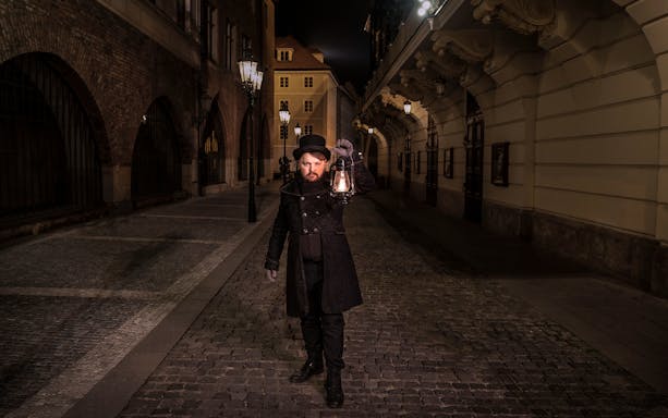 Guide holding lantern on cobblestone street during Prague Old Town ghost tour.