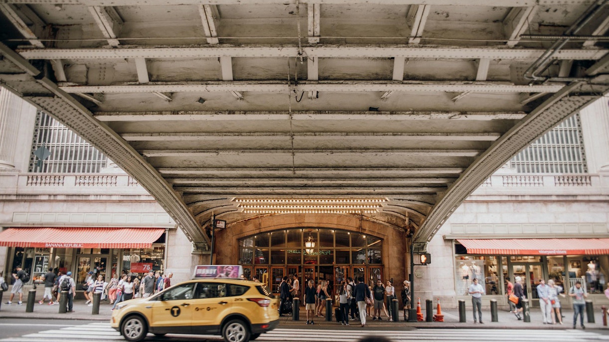 Grand Central Terminal entrance with people and a yellow taxi on a walking tour.