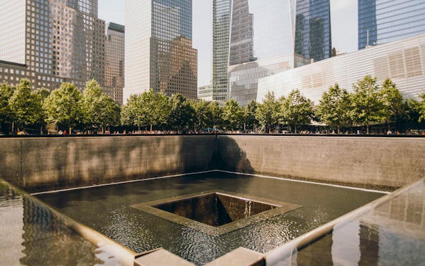 9/11 Memorial reflecting pool with surrounding skyscrapers in New York City.
