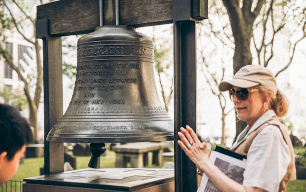 Tour guide explaining the significance of the Bell of Hope at the 9/11 Memorial in New York City.