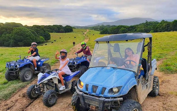 Visitors riding ATVs and a buggy on a trail at KUR-Cow Farm, surrounded by lush fields and distant hills.