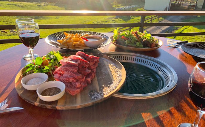 Waygu beef and salad on a table with wine, overlooking a green pasture in Kuranda.
