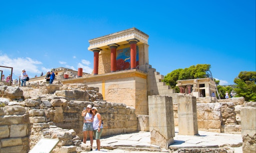 Visitors exploring Knossos Palace ruins in Heraklion, Greece, with audio tour guide.