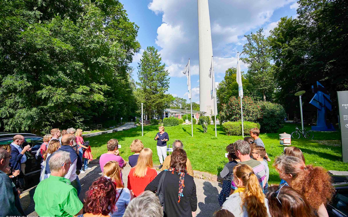 Group tour at the base of Fernsehturm Stuttgart, guide speaking to visitors.