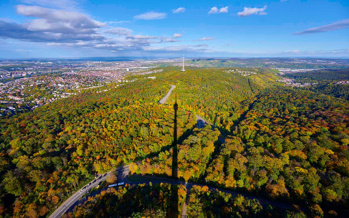 Aerial view of Stuttgart with Fernsehturm shadow over forested hills.