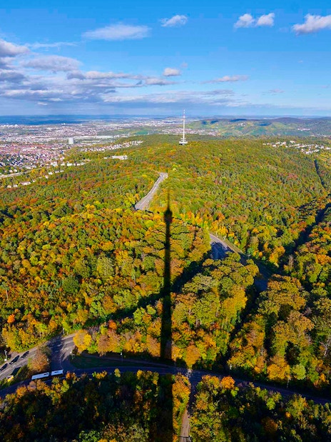 Aerial view of Stuttgart with Fernsehturm shadow over forested hills.