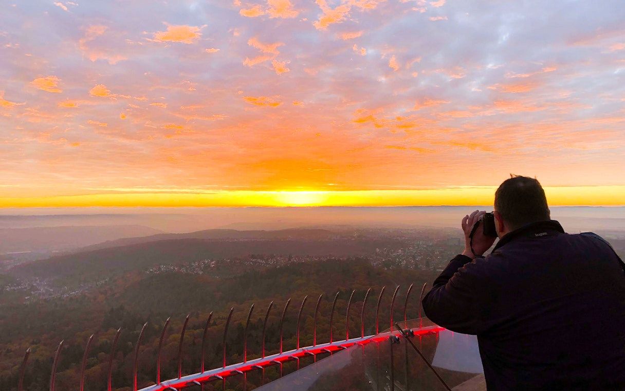 Person photographing sunset from Fernsehturm Stuttgart observation deck.