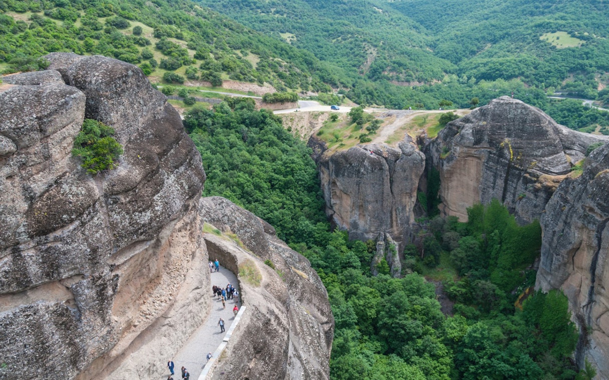 Hikers on a narrow path along Meteora's rocky cliffs, Greece.