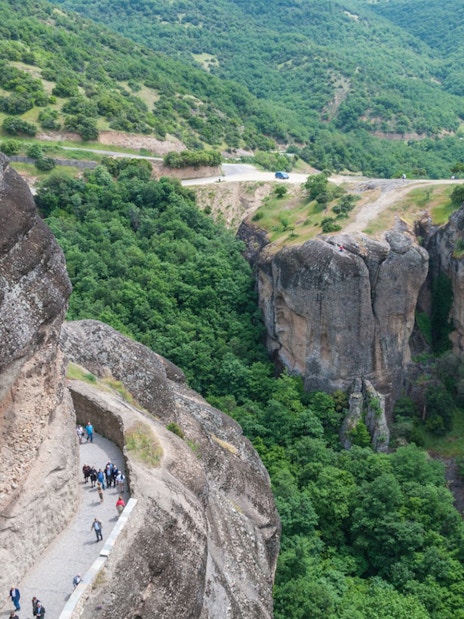 Hikers on a narrow path along Meteora's rocky cliffs, Greece.