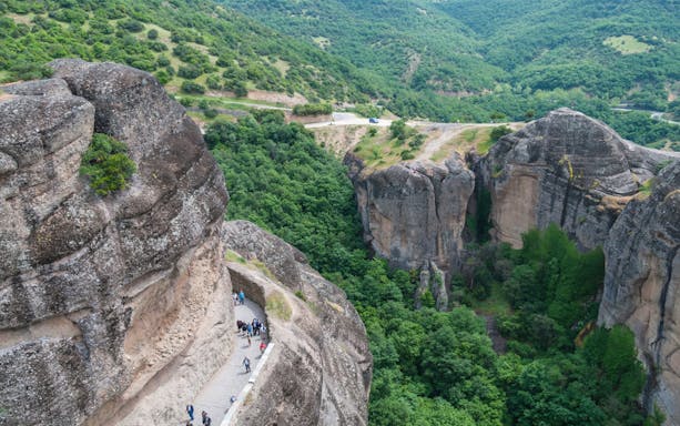 Hikers on a narrow path along Meteora's rocky cliffs, Greece.