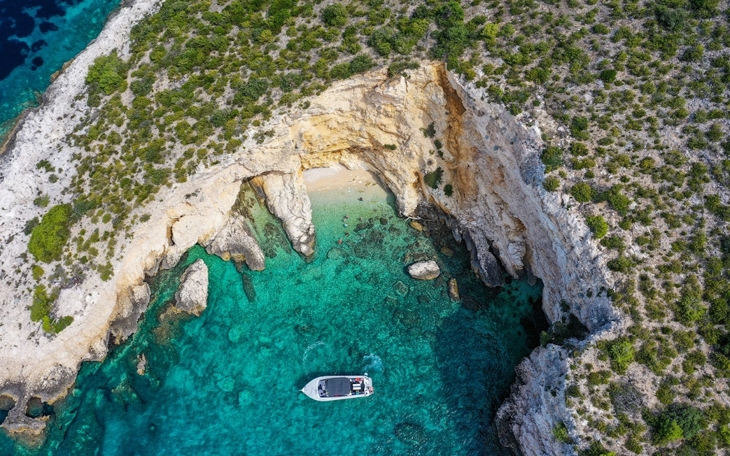 Boat near rocky coastline with clear turquoise water on Split tour to Blue Cave, Vis, and Hvar.