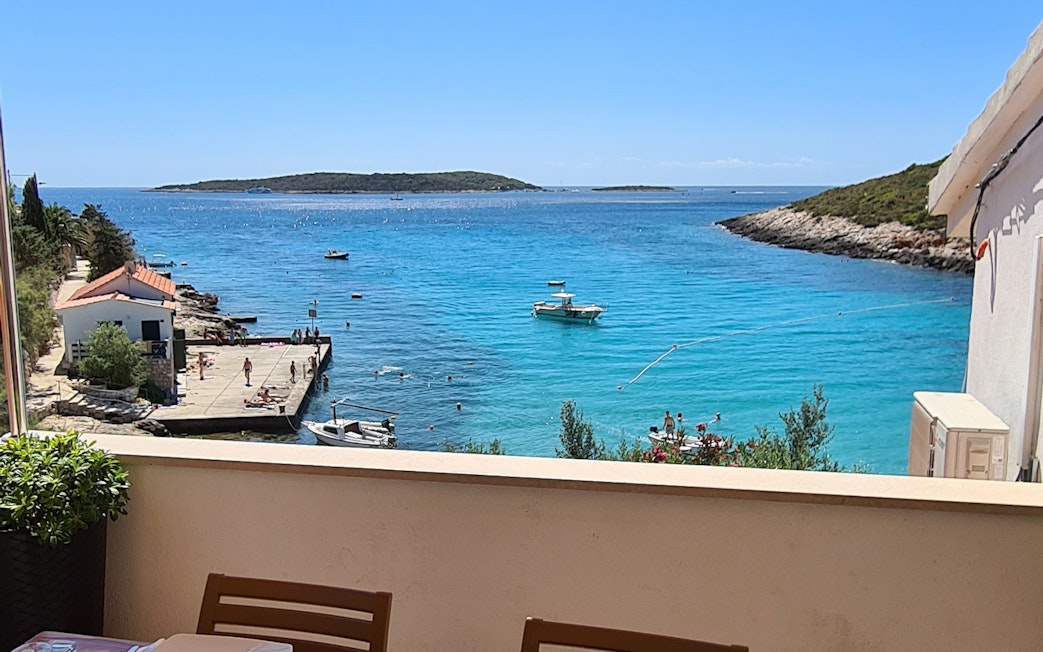 Boats and swimmers in clear blue water near a dock on Vis Island, Croatia.