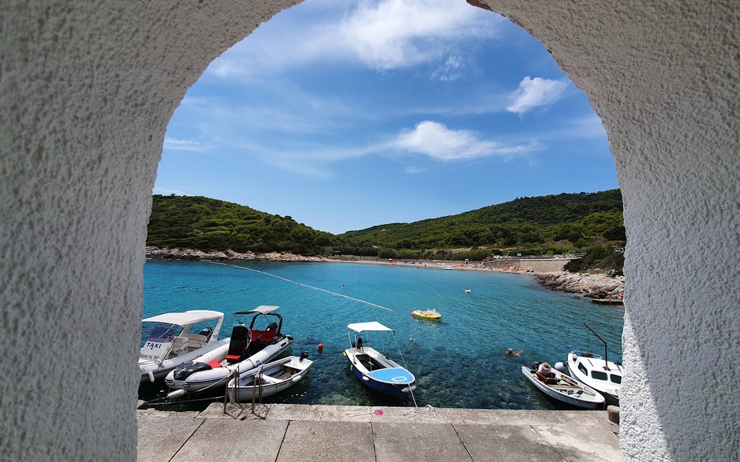 Boats docked in a turquoise bay on Vis Island, Croatia, viewed through an archway.