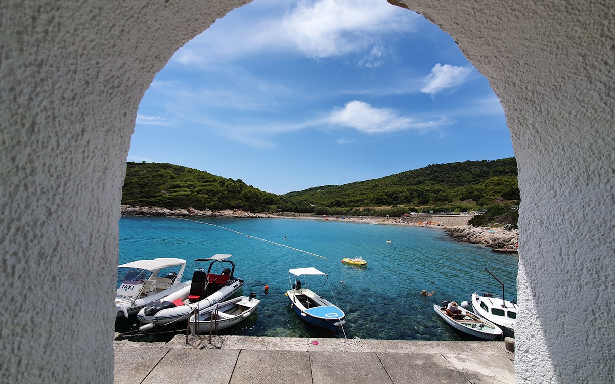 Boats docked in a turquoise bay on Vis Island, Croatia, viewed through an archway.