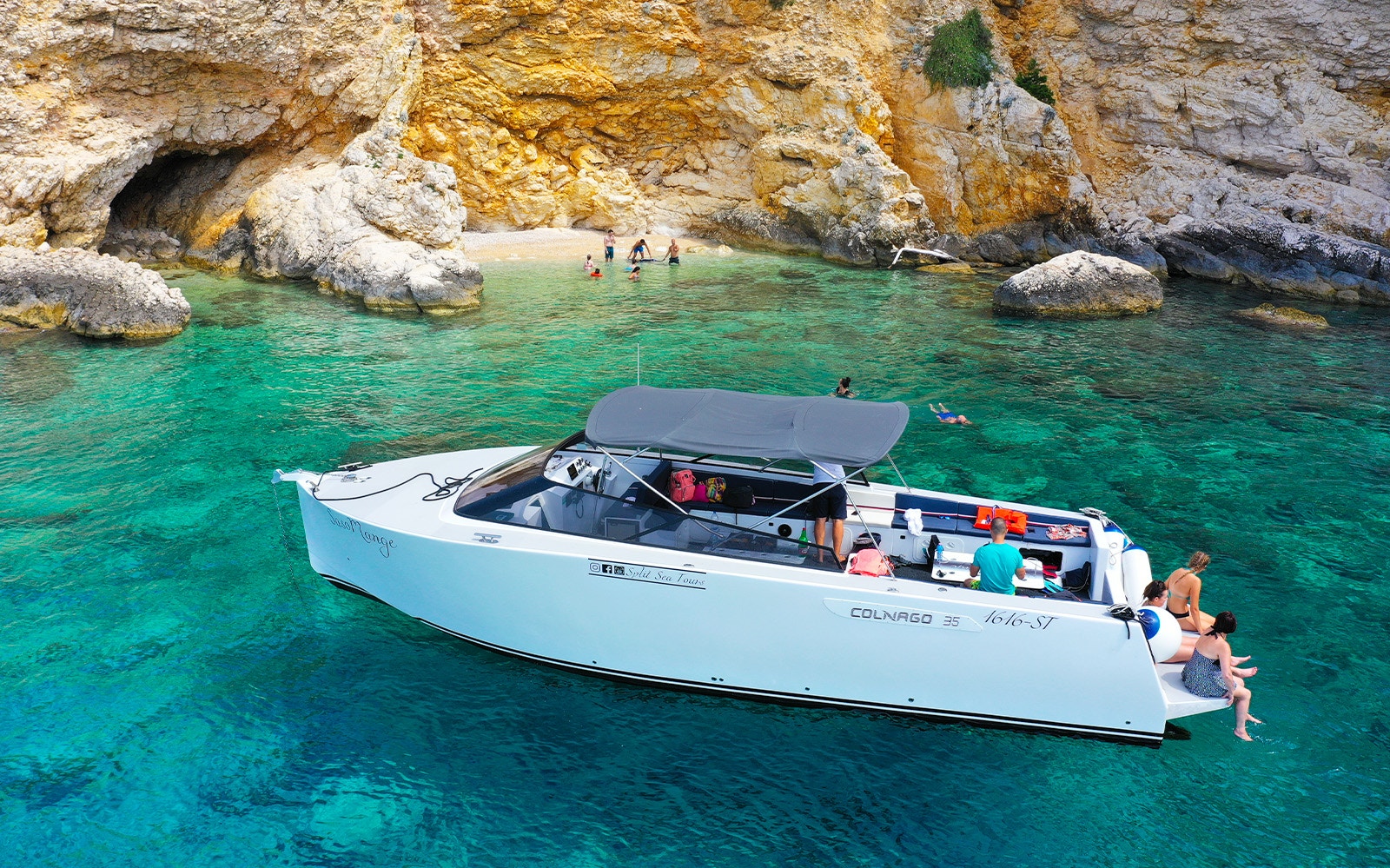 Boat near rocky shore with people swimming, part of Split's Blue Cave, Vis, and Hvar tour.