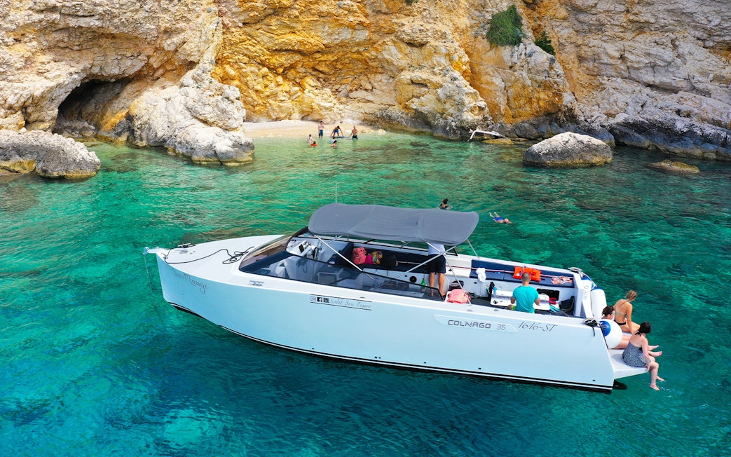 Boat near rocky shore with people swimming, part of Split's Blue Cave, Vis, and Hvar tour.
