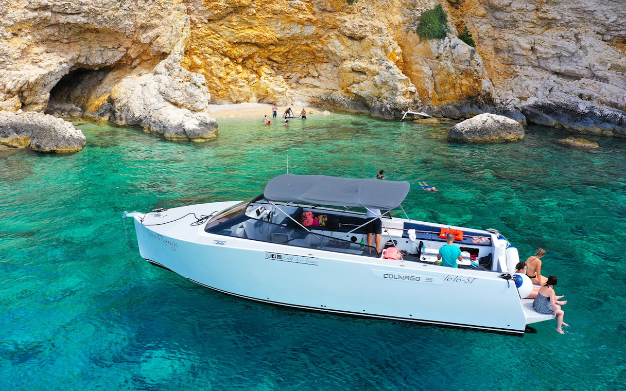 Boat near rocky shore with people swimming, part of Split's Blue Cave, Vis, and Hvar tour.