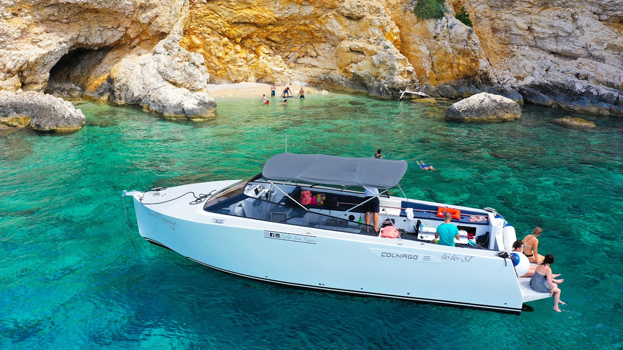 Boat near rocky shore with people swimming, part of Split's Blue Cave, Vis, and Hvar tour.