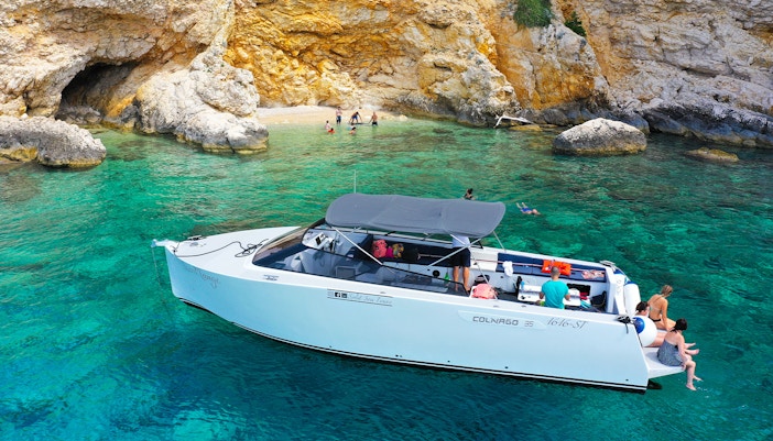 Boat near rocky shore with people swimming, part of Split's Blue Cave, Vis, and Hvar tour.