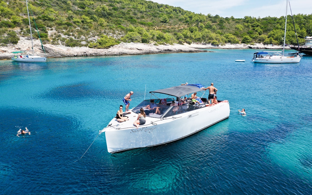 Boat tour with people swimming near Vis, Croatia, surrounded by clear blue water and lush coastline.