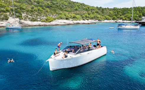 Boat tour with people swimming near Vis, Croatia, surrounded by clear blue water and lush coastline.