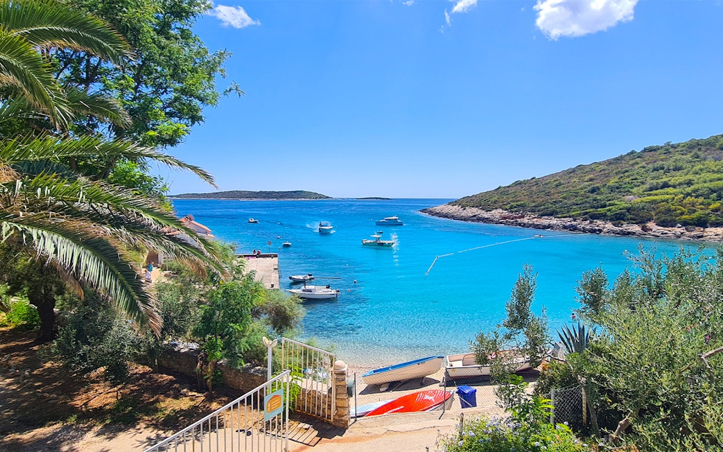 Boats anchored in a turquoise bay near Split, Croatia, with lush greenery and a clear sky.
