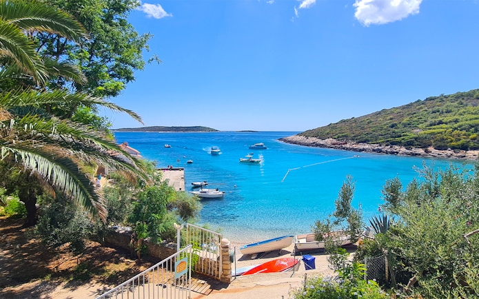 Boats anchored in a turquoise bay near Split, Croatia, with lush greenery and a clear sky.