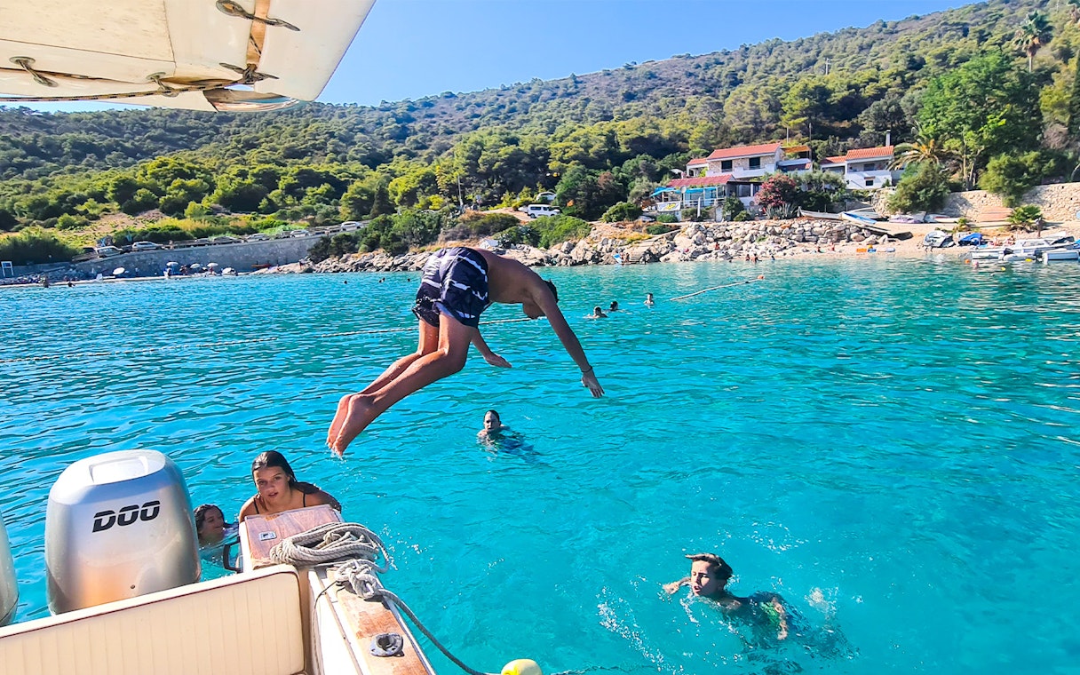 Person diving off a boat into clear blue water near Vis, Croatia, with swimmers nearby.