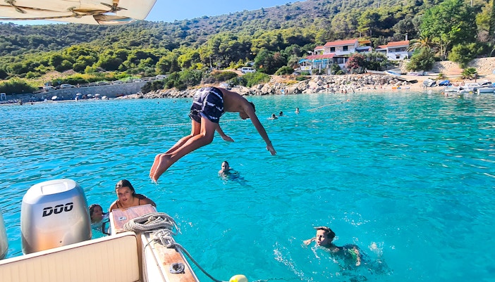 Person diving off a boat into clear blue water near Vis, Croatia, with swimmers nearby.