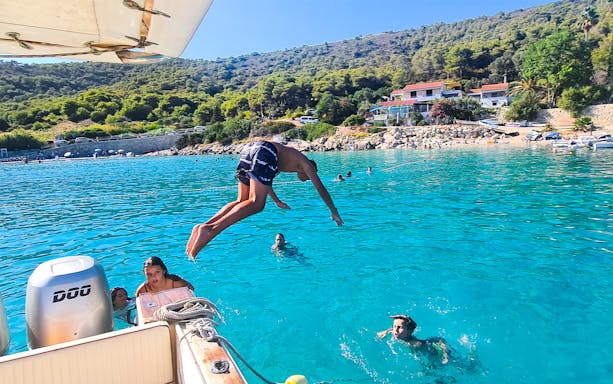 Person diving off a boat into clear blue water near Vis, Croatia, with swimmers nearby.