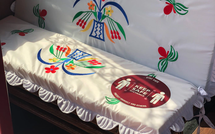 Embroidered seat cover with floral design and social distancing sign on a cultural tour bus.