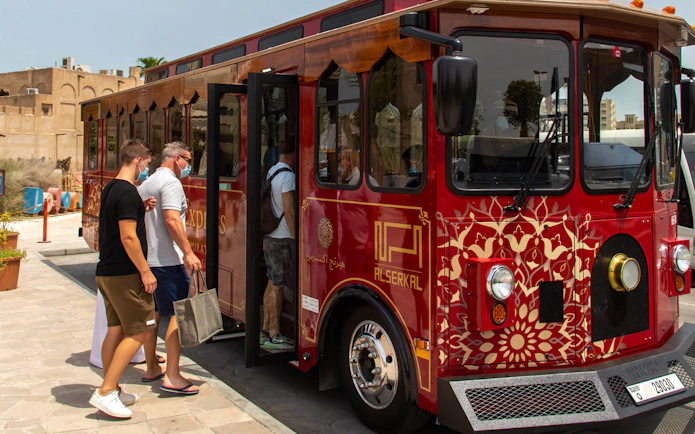 Tourists boarding a red cultural tour bus in Dubai.