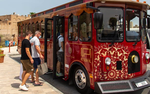 Tourists boarding a red cultural tour bus in Dubai.