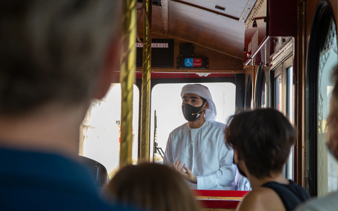 Tour guide in traditional attire speaking to tourists on a cultural bus tour.