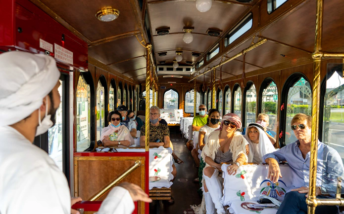 Tourists on a cultural tram tour in Dubai, guided by a local in traditional attire.